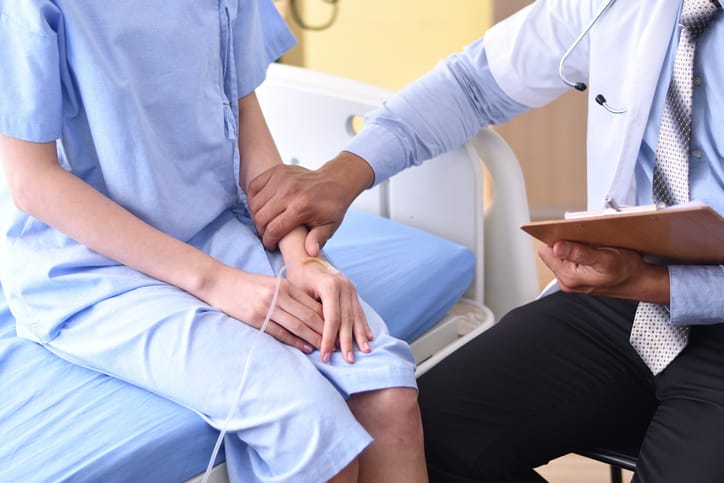 Photo shows a doctor touching the arm of a patient in a hospital/Getty Images