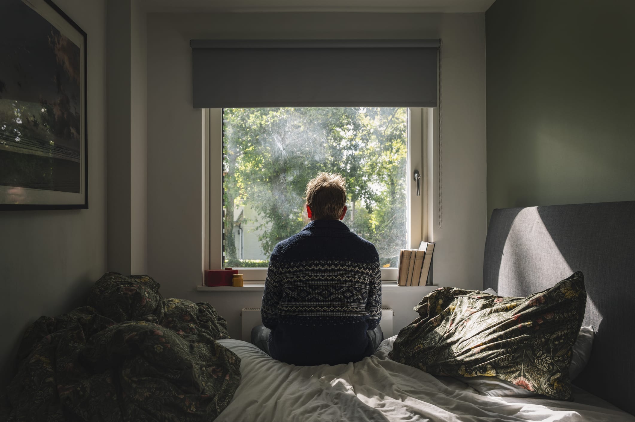 Man sitting on bed while sun streams in through the window