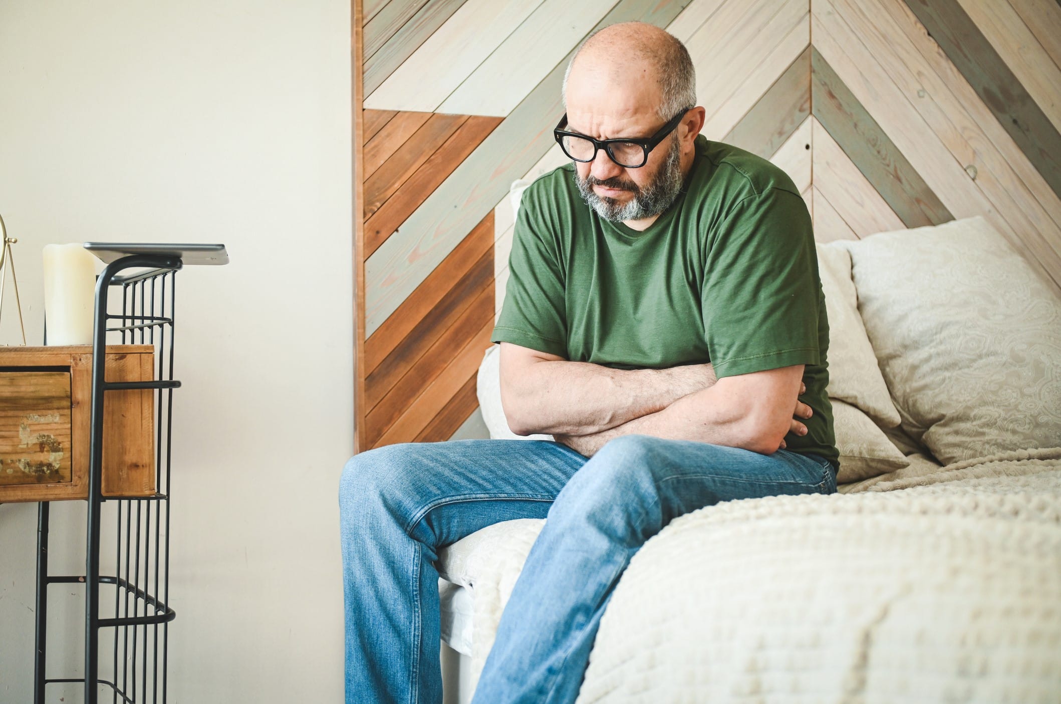 Man sitting on bed clutching abdomen in pain