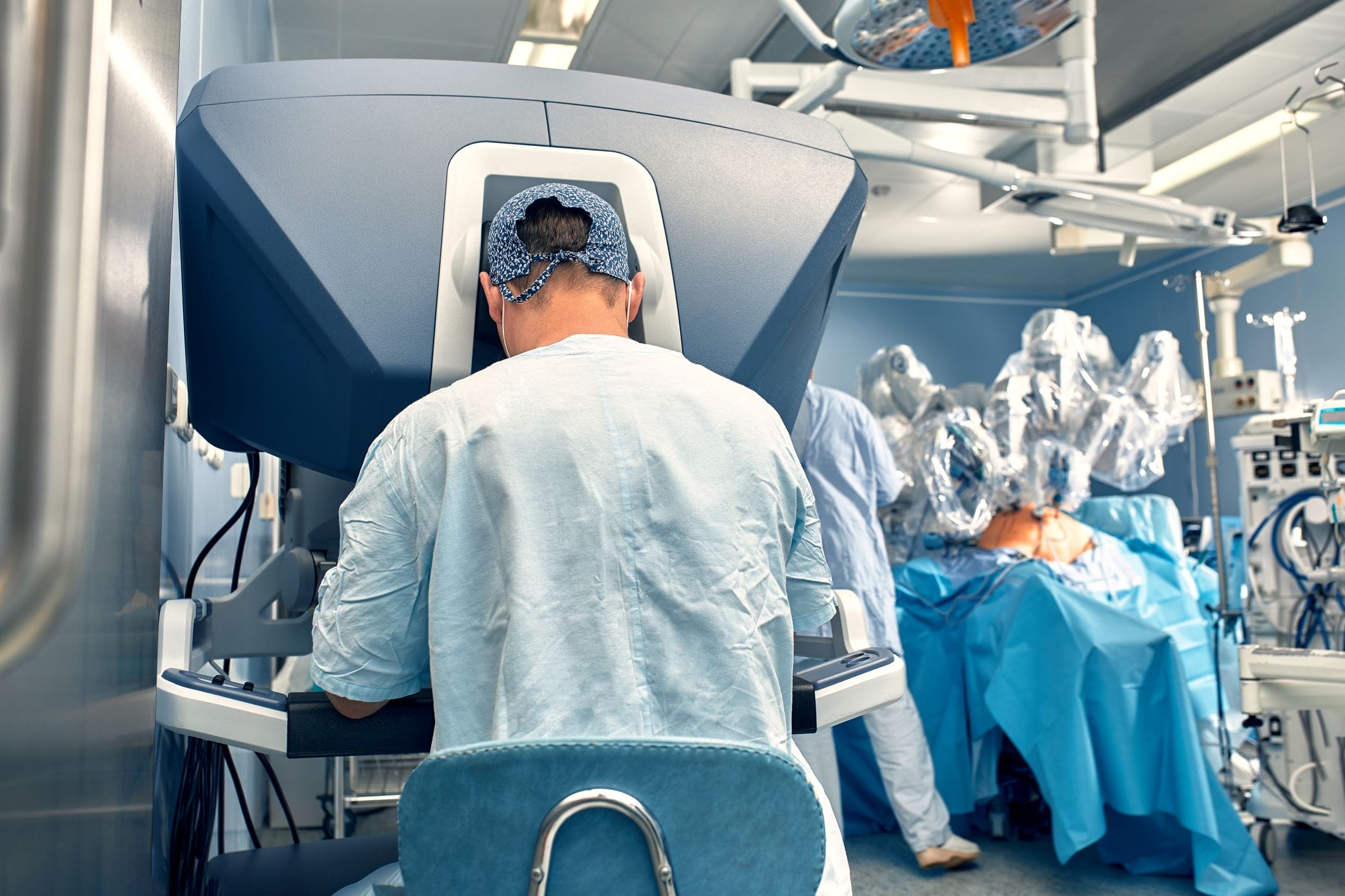 Surgeon performing robot-assisted surgery with patient in background