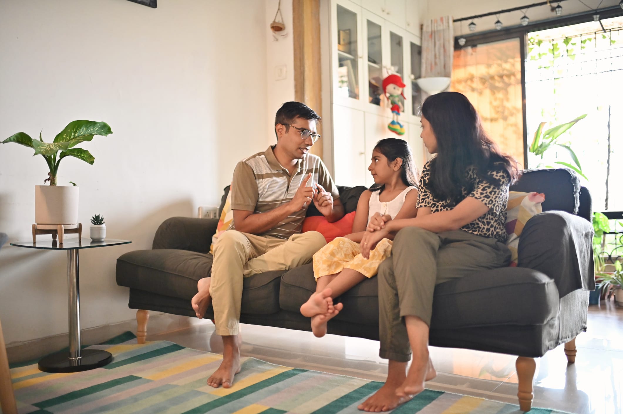 Parents sitting on sofa with their daughter on a sofa and talking to her